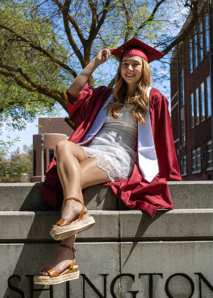 A girl in a white dress and a red cap and gown touches her cap