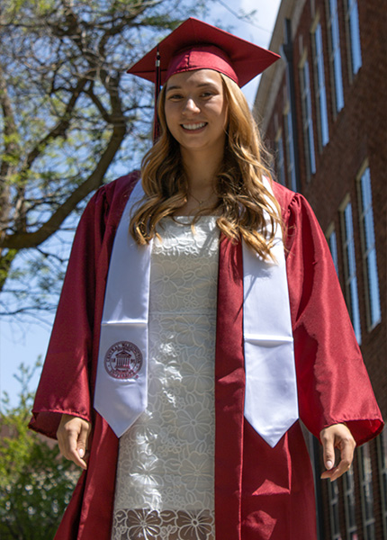 A girl in a white dress and a red cap and gown smiles for a photo