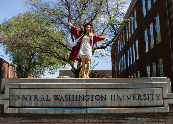 A girl in a white dress and a red cap and gown hugs her childhood stuffed animal
