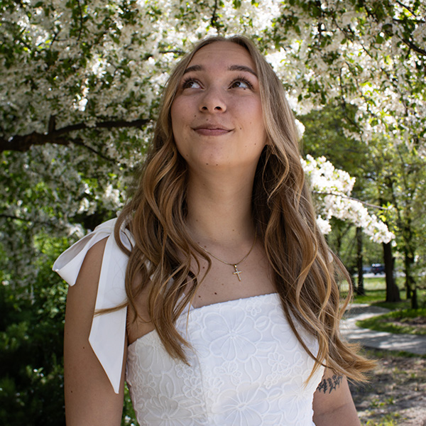 A girl in a white dress stands under a white cherry blossom tree