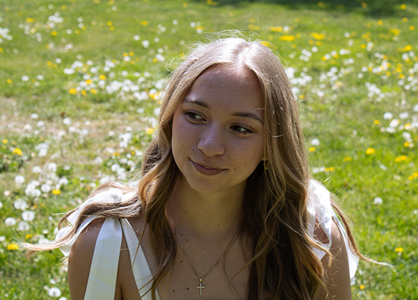 A girl in a white dress sits in a field of flowers looking to the side