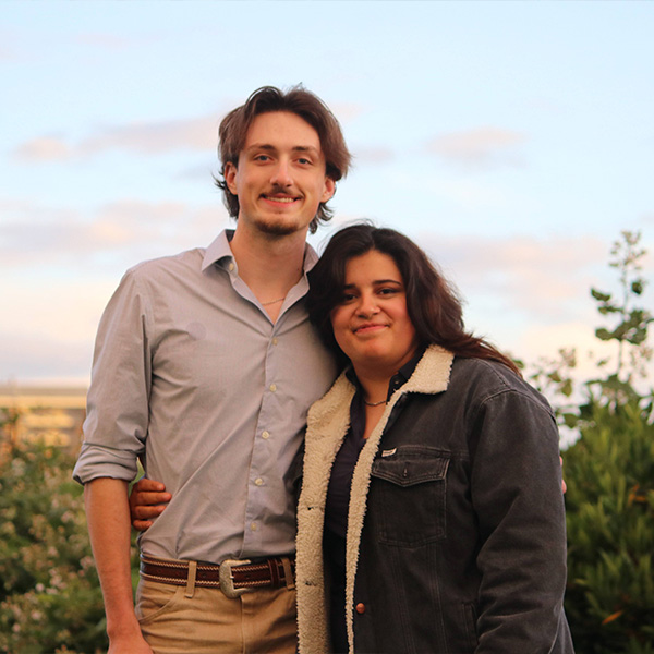 Close up of a young couple facing the camera smiling, posed in a side embrace