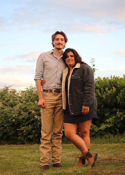 A young couple facing the camera smiling, posed in a side embrace