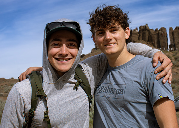 Two young men face the camera smiling with arms around each others shoulders